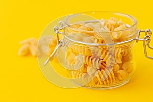 Closeup of fusilli pasta in galss jar on yellow background