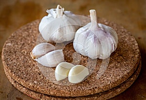 Closeup of garlic bulb and cloves on a round cork board