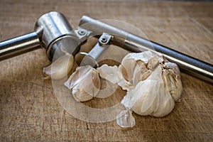 Closeup of a garlic press and fresh garlic on a wooden table