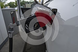 Closeup of gas station pump gun nozzle inserted into a car fuel tank filling up gasolin