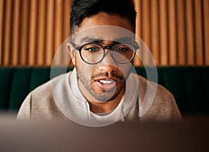 .. Closeup of geeky young indian man wearing glasses while reading something interesting and sitting inside. Man wearing