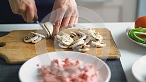 Closeup of girl hands cutting the mushrooms on wooden board for pizza in the kitchen at home