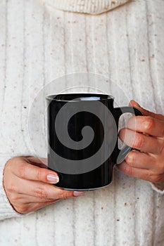 Closeup of girl holding blank black coffee mug mockup. Dark mug mock up for your company logo and design