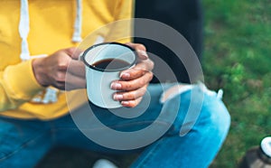 Closeup girl holding in hands cup of hot tea on green grass in outdoors nature park, beautiful woman hipster enjoy drinking cup