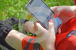 Closeup of a girl searching something on her phone, iphone while sitting on the grass in a park