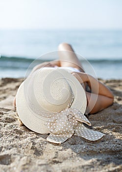 Closeup of girl in swimsuit and hat taking sunbath at sandy beach