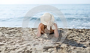 Closeup of girl in swimsuit and hat taking sunbath at sandy beach