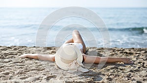 Closeup of girl in swimsuit and hat taking sunbath at sandy beach