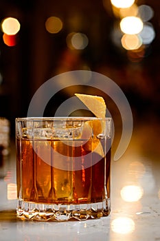 Closeup glass of godfather cocktail with slice of orange and ice cubes at bright bar background