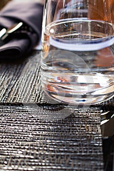 Closeup of a glass of purified fresh drinking water without gas on a table with a reflective surface with a napkin and cutlery.
