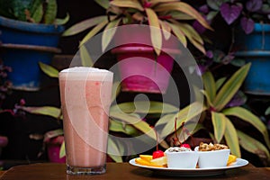 Closeup of a glass of a strawberry milkshake served with a plate of fruits and pastry