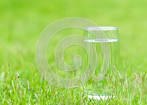 Closeup glass of water on green grass nature background, food healthy concept