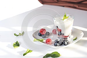 `Closeup glass of yogurt with fresh berries and mint on the white plate.