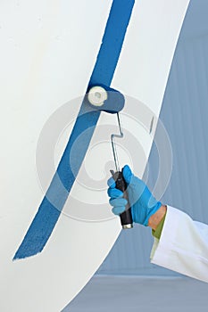 Closeup of gloved hand painting a boat with antifouling paint using a roller