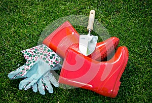 Closeup of gloves, gumboots and shovel on green grass