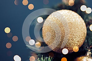 Closeup of gold bauble hanging from a decorated Christmas tree