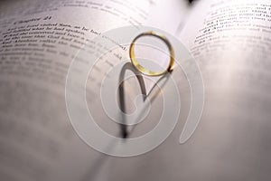 Closeup of a golden engagement ring forming a shadow of a heart on the open holy bible