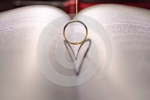 Closeup of a golden engagement ring forming a shadow of a heart on the open holy bible