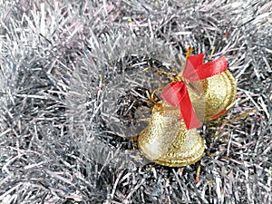 Closeup of golden jingle bells with red ribbon on a silver background.