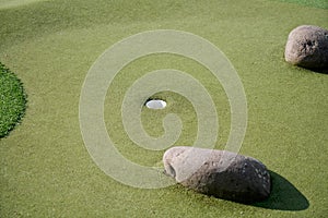 Closeup of a golfing club with rocks, grass and the hole for the golf ball