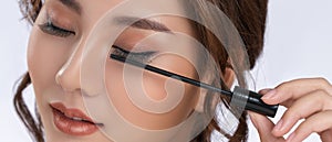 Closeup gorgeous young woman putting black mascara on her eyelashes with brush.