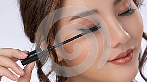 Closeup gorgeous young woman putting black mascara on her eyelashes with brush.