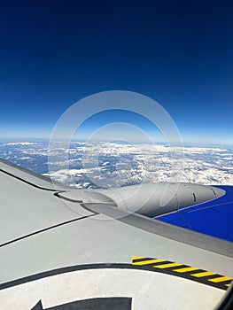 Closeup of gray airplane wing flying high in the blue sky