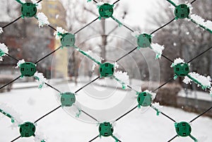 Closeup of a green chain-link fence in a forest covered in the snow in winter