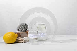 Closeup of green cleaning products on the white table.Glass jars of vinegar and backing soda, organic soap, lemon against white wa
