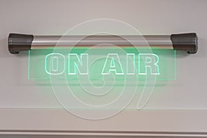 Closeup of a green neon On Air sign on the white wall of a radio studio
