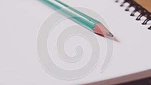 Closeup of a green pencil on a notebook. Notepad open on a blank page on the table