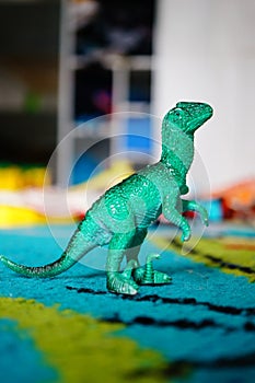 Closeup of a green toy dinosaur on a blue carpet under the lights with a blurry background