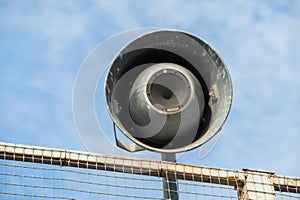 A closeup of a grey loudspeaker hanging from a metal net