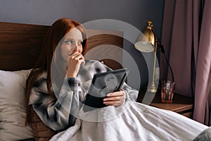 Closeup of grief-stricken young woman lying on bed under blanket holding photo in frame and crying looking away