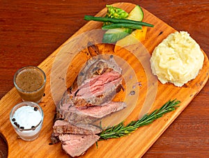 Closeup of grilled beef steak with mashed potatoes and vegetables on a wooden board