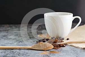 Closeup ground coffee in wooden spoon and fresh roasted coffee beans with a cup of hot coffee.