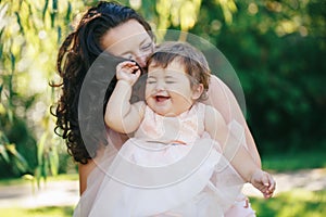 Closeup group portrait of beautiful white Caucasian brunette mother holding laughing baby daughter kissing her in cheek