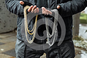 Closeup of a guy in black grungy outfit, holding silver and golden chains