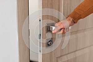 Closeup of guy opening wooden door, holding hand on handle