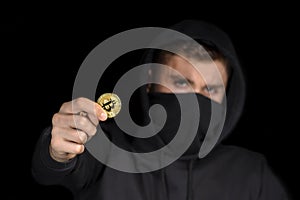 Closeup hacker with blurred face hold bitcoin in hand initiating cyber attack, concept cyber security,  on black
