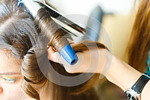 Closeup of hairdresser doing the styling for a festive evening of wedding hairstyles woman with long black hair