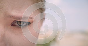 Closeup half face portrait of young cute caucasian female face with eye looking at camera with disappointment outdoors