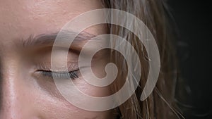 Closeup half-face shoot of young pretty caucasian brunette female face with brown eye being closed in front of the