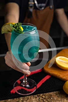 Closeup of the hand of a barman holding a blue colored cocktail in his hand