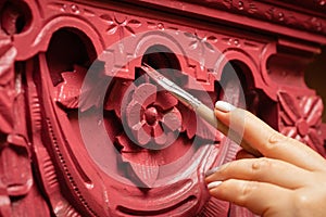 Closeup of hand carefully painting amazing ornaments on wooden cupboard in red color with brush. Home workshop for