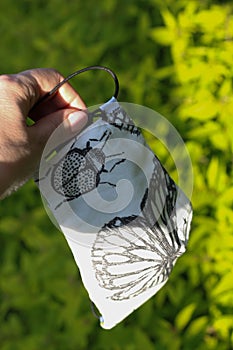 Closeup hand catch flying face mask with gray Butterfly. To protect from coronavirus, virus concept. Garden in spring, summer.