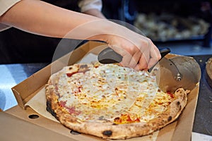 Closeup hand of chef baker in white uniform cutting pizza at kitchen.