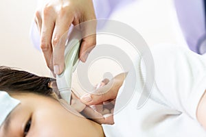 Closeup of hand doctor or nurse checking child patient temperature in the ear using digital thermometer,asian little girl having