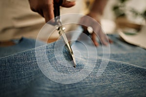 Closeup of hand of fashion designer using a scissor to cut a fabric sample. Tailor cutting a piece of denim material