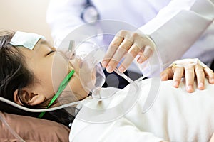 Closeup of hand female caregiver holding oxygen mask with cute child patient in hospital bed or home,little girl putting